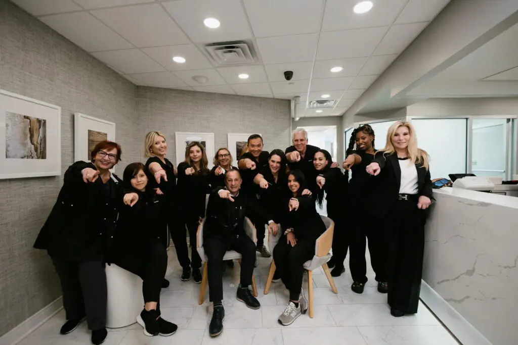 The Manhattan Dental Spa team in black shirts pointing at the camera
